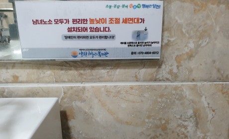 높낮이 조절 세면대 앞 거울에 부착된 안내문구 '남녀노소 모두가 편리한 높낮이 조절 세면대가 설치되어 있습니다'