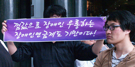 껌 값으로 장애인 우롱하는 장애인연금제도 기만이다. 작은현수막을 들고 있는 사진 